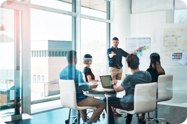 Man at a white board in front of a collaborative team session